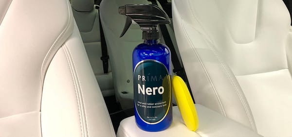 A bottle of Prima Nero car care product sits on the console of a white vehicle interior